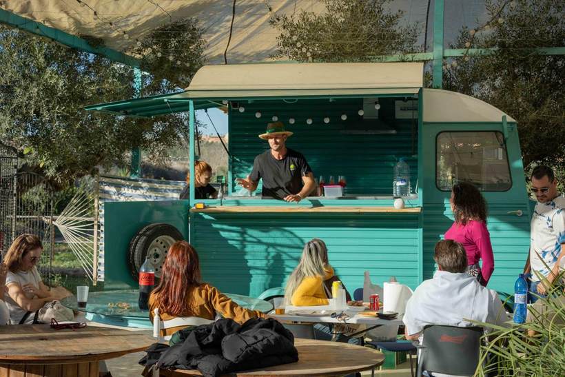 Foodtruck turquesa de Ecoland con mesas a la sombra de los olivos en la finca de Pilar de la Horadada